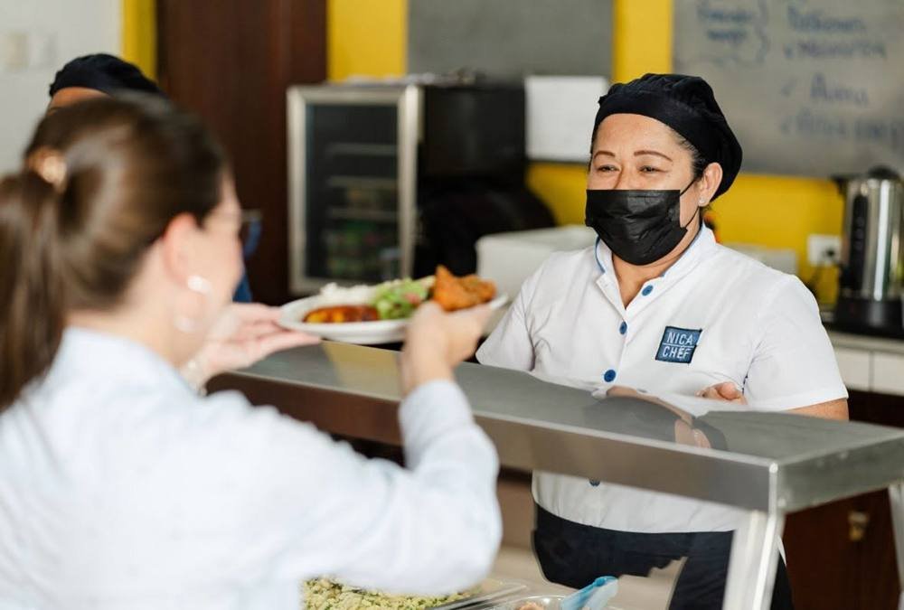 Integrante del equipo de NicaChef con uniforme sirviendo un plato en el buffet