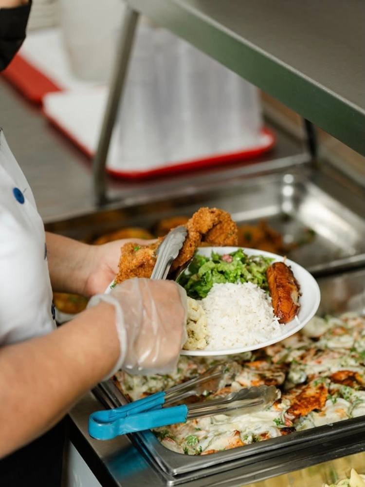 Plato de arroz, ensalada y pollo empanizado servido en la línea de buffet