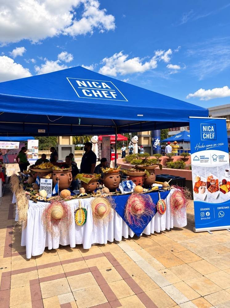 Stand de NicaChef en un evento al aire libre, con carpa azul y mesa decorada con ollas de barro
